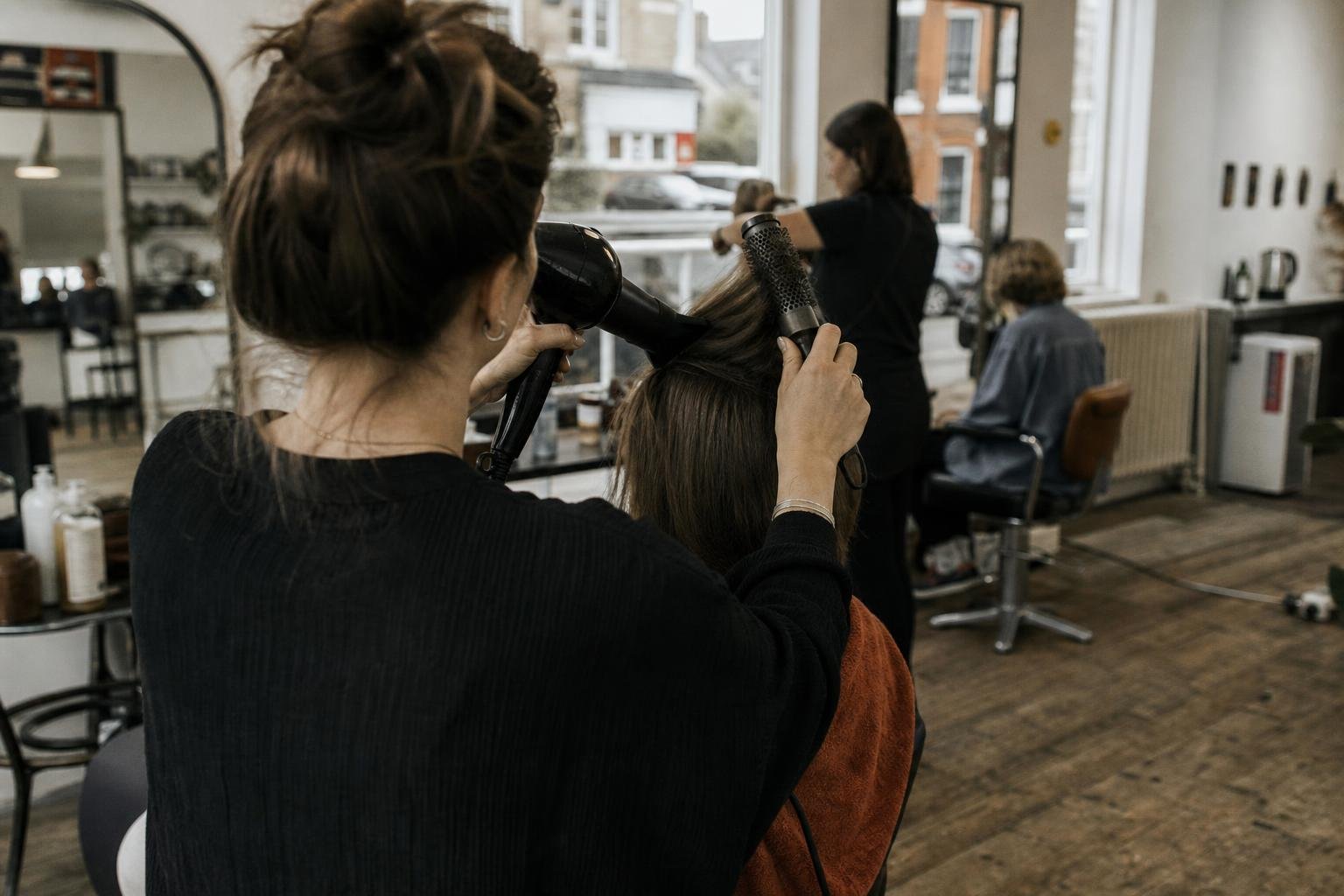 A hairdresser mid blow-dry in a busy independent salon, the sort of shop Google Ads for hairdressers is meant to fill