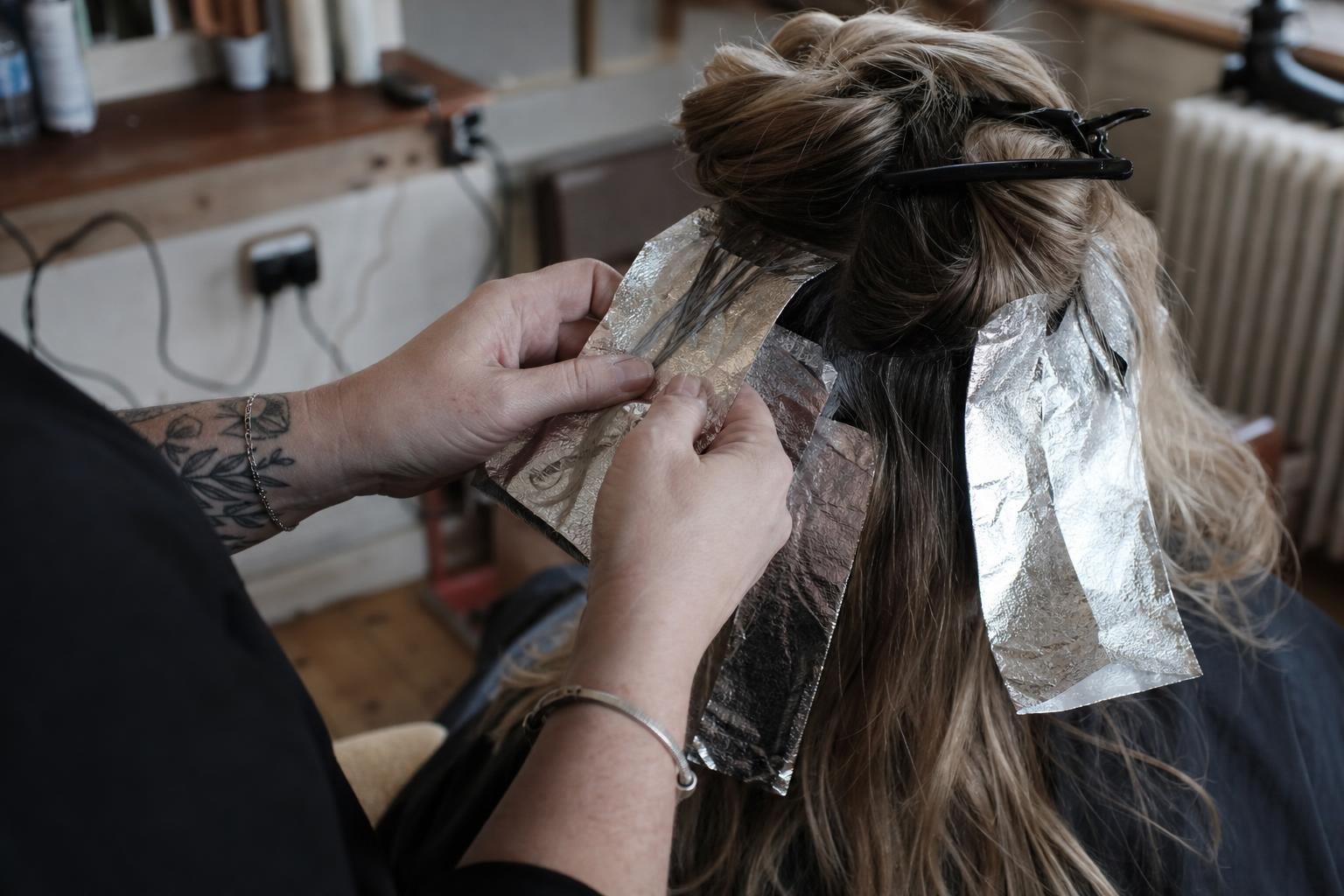 A stylist's hands folding foils through a client's hair, the colour work a Google Ads credit offer has to pay for