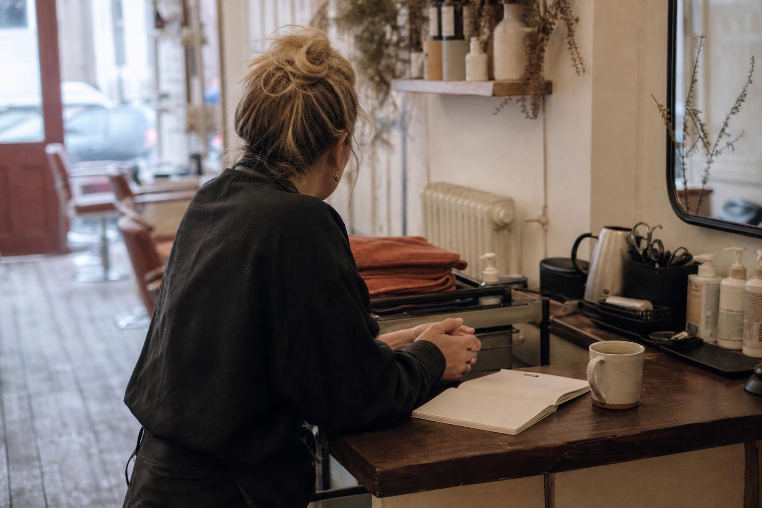 A salon owner leaning on the counter with a notebook, working out how much a salon should spend on Google Ads