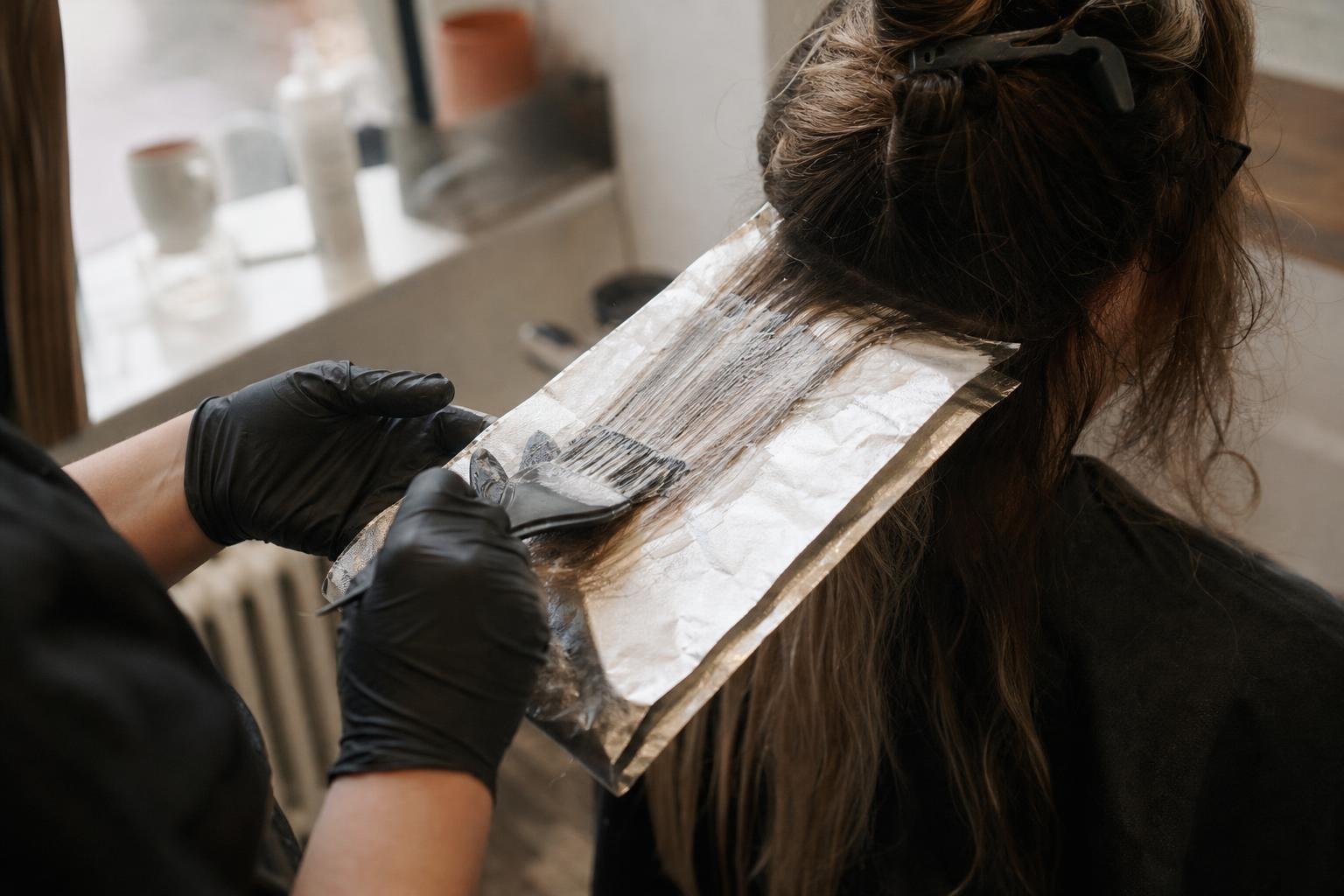 A colourist's gloved hands painting balayage over a foil, the kind of colour booking a Google ad is meant to bring in