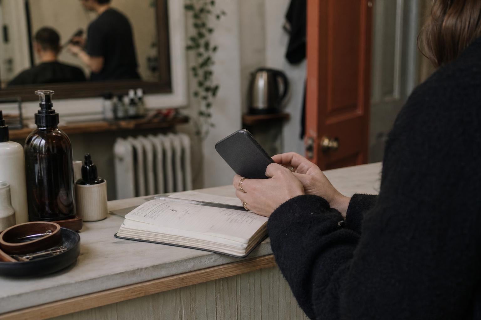 Hands holding a phone at a salon counter beside an open paper appointment diary