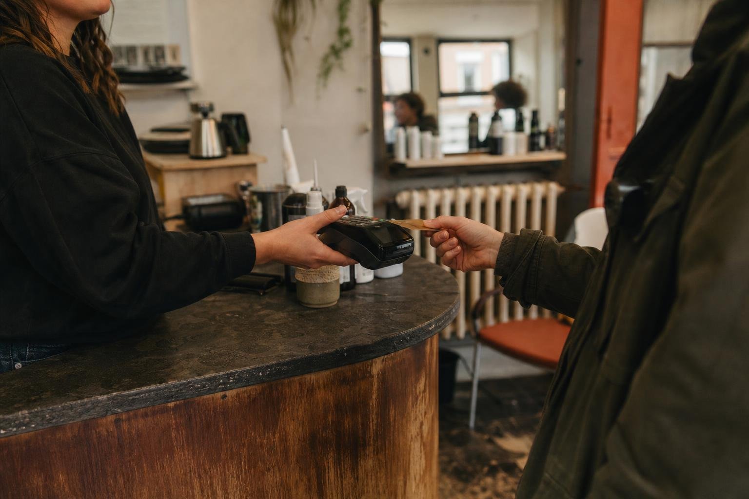 A client handing a card to a machine held out across a salon counter