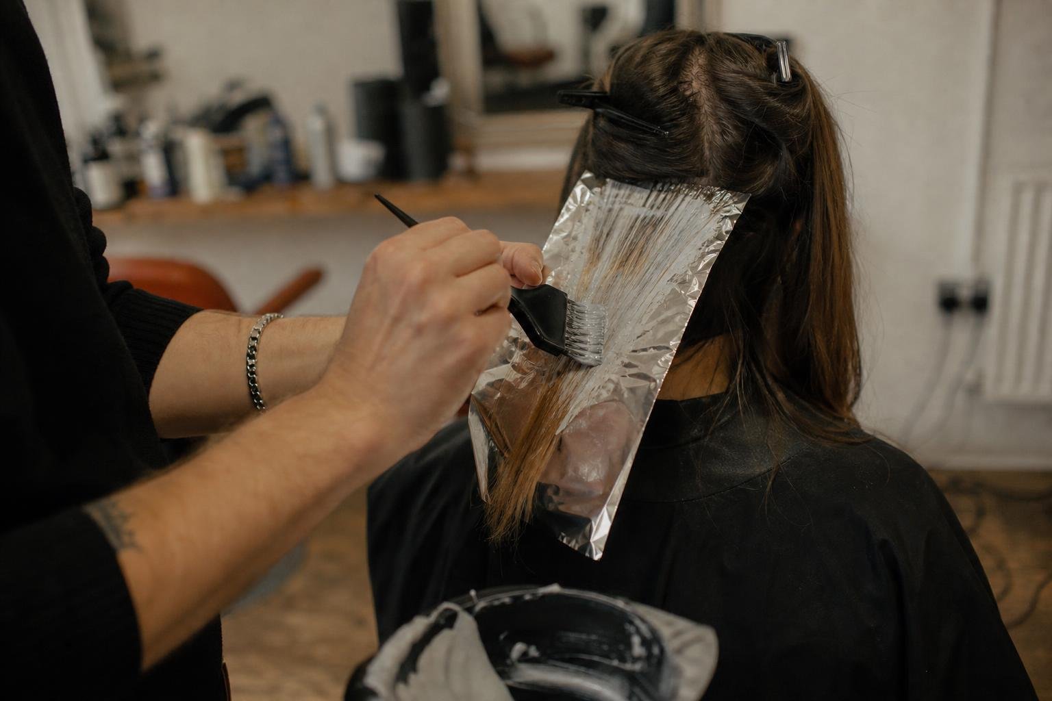 A stylist's hands painting colour onto a foil section, the higher-bill work that matters most for a salon near the VAT threshold