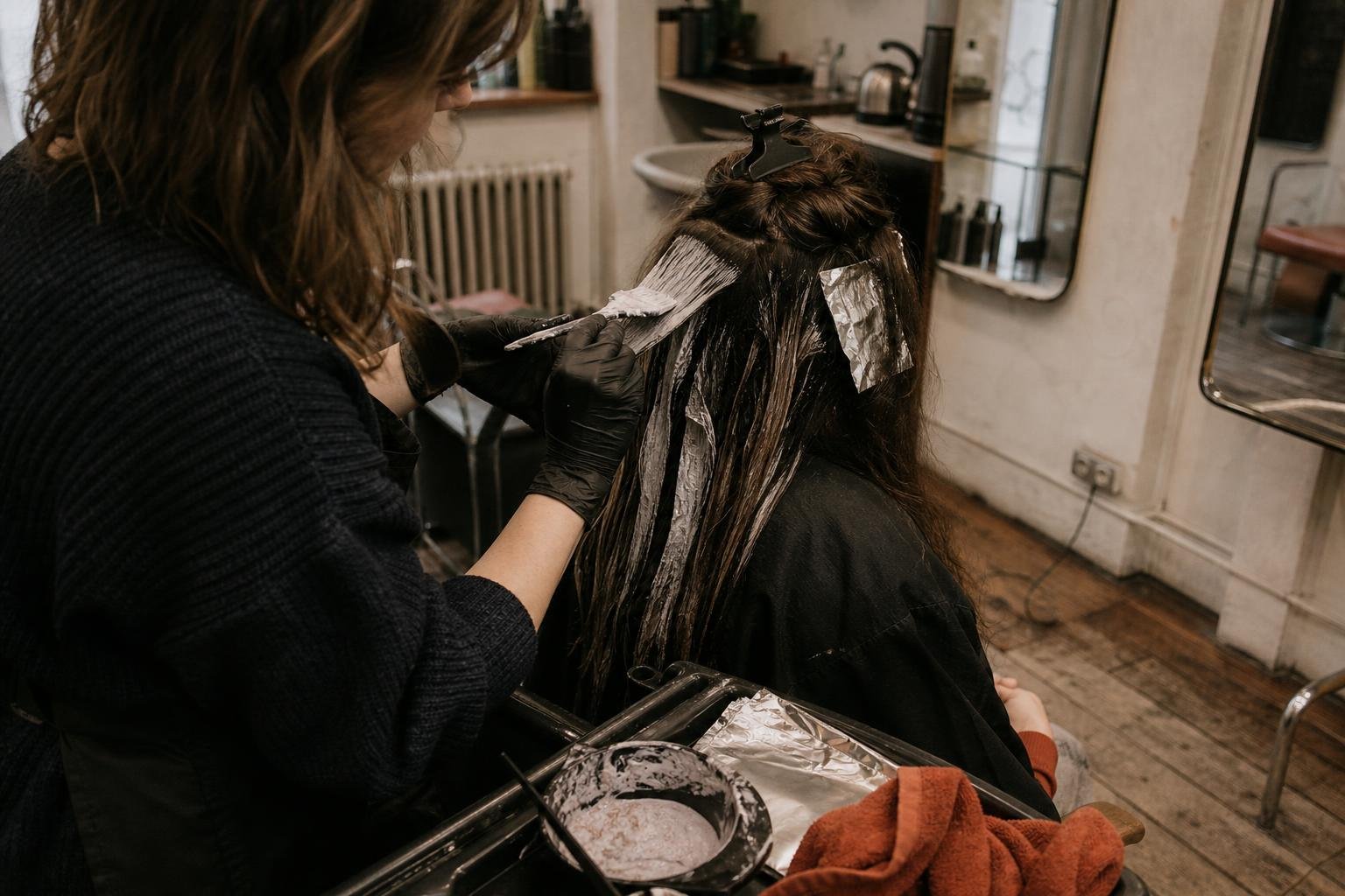 A stylist's gloved hands painting colour through a client's mid-lengths in the kind of salon a new salon nearby competes with