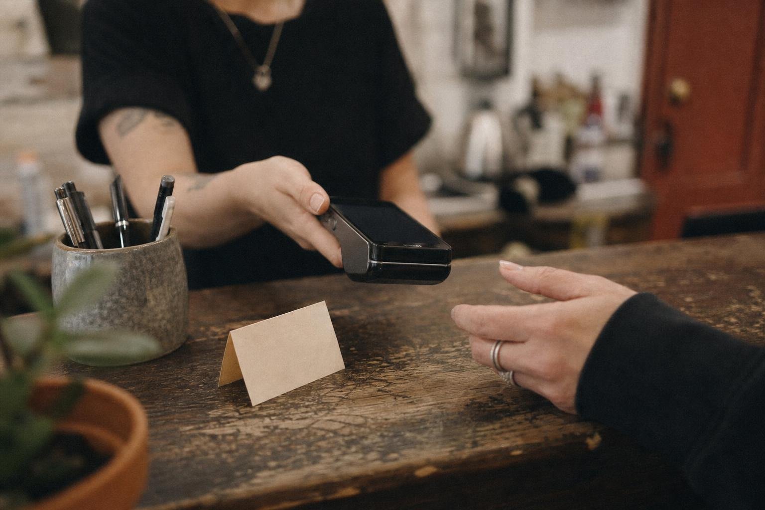 Hands passing a card machine across a worn salon reception counter beside a blank appointment card